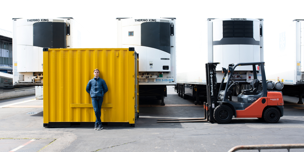 An environmental portrait of Daan for Grip op Finance, photographed at the RAI grounds in Amsterdam. The image achieves balance through the use of primary colors: the yellow square container, Daan’s blue jacket, and the red side of the forklift.
