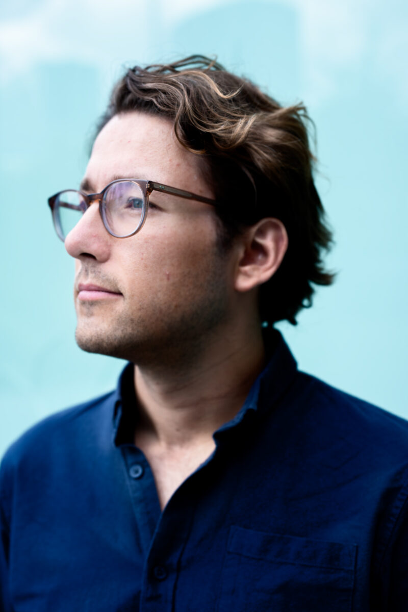 Een portret van Krisjan Oldekamp voor een turquiose achtergrond buiten gemaakt