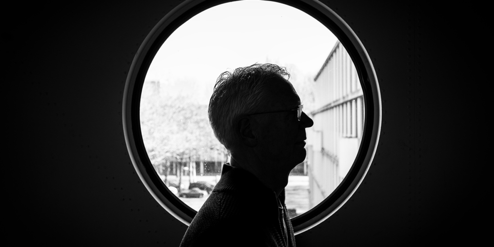 This is an environmental portrait of Rob. It's black and white in front of a circular window. The location is Het breed or Plan van Gool.
