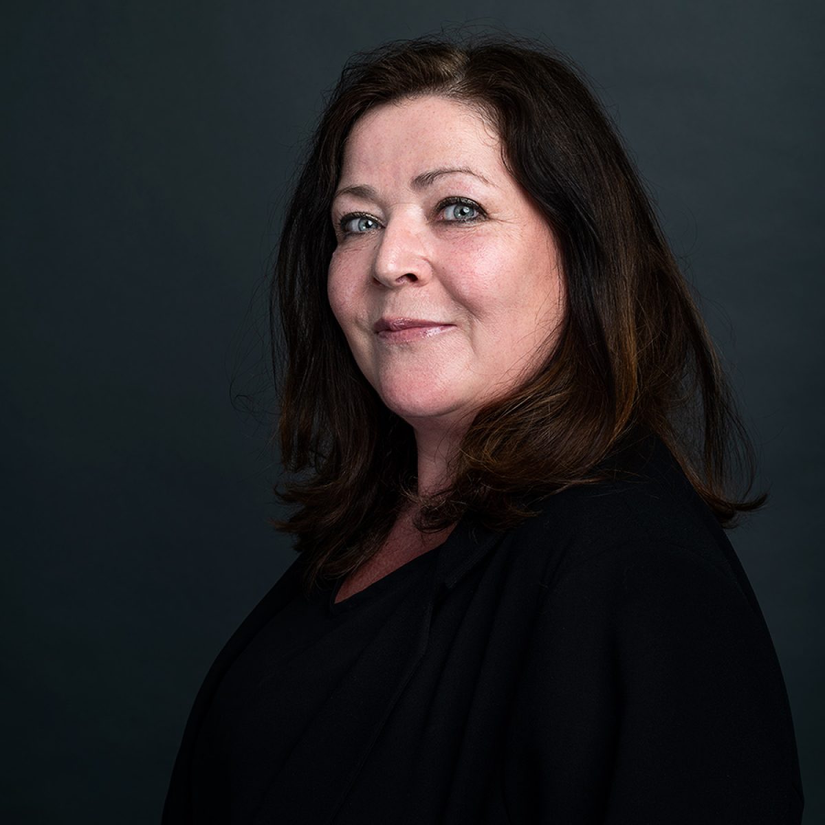 Portret van Ulli, medewerker van TCC Global, tegen een rustige donkere achtergrond met zacht licht dat haar gezicht helder en vriendelijk in beeld brengt.